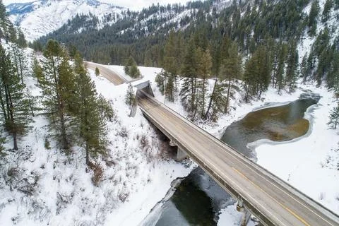 Winter road bridge over river surrounded by snow-covered pine trees Stock Photos