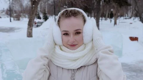 Winter scene featuring smiling young woman wearing white earmuffs and warm scarf Stock Photos