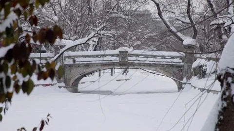 Winter scene with people walking on park bridge over frozen lake during blizzard Stock Footage 71965565