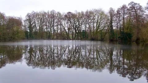 Winter scene showing trees reflected in still water of English lake Stock Photos