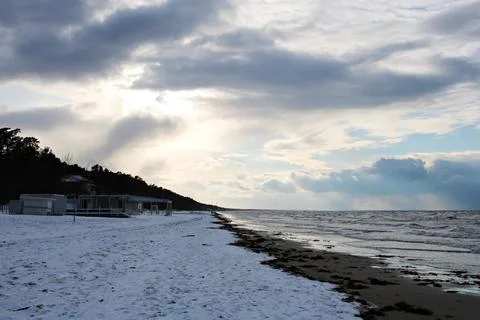 Winter sky with dark clouds and the sea coast covered with snow Stock Photos
