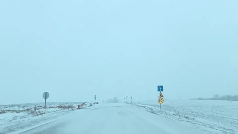 Winter snow covers empty road with signs showing speed limits in rural area duri Stock Footage 326694923
