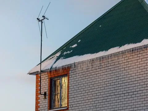 Winter snow melts down a green roof. Icicles hang from the eaves. Window gl.. Stock Photos