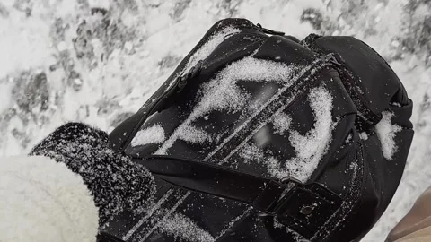In winter, in snowfall, a man carries a black leather travel bag Vidéo 258069708