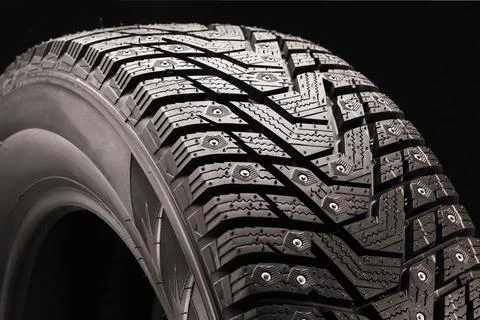 Winter studded tire side view close-up on a black background Stock Photos