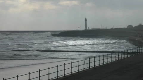 Winter sun light on silvery waves, silhouetted promenade railing and lighthouse Stock Footage 1097629
