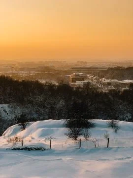 Winter sunset casting warm glow over snow covered hills, trees, and buildings in Stock Photos
