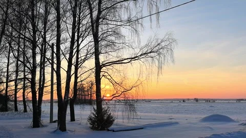 Winter sunset over snow-covered fields with trees in the foreground Stock Footage 327103395