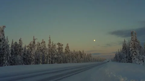 Winter sunset over a snowy road in northern landscape featuring tall trees and a Stock Footage 284434629