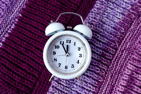 Winter is the time for needlework: white clock on a lilac knitted product, cl Stock Photos