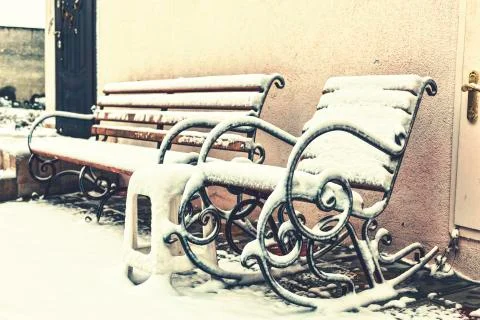 Winter time. Snow-covered bench and rocking chair in the courtyard of the hou 写真素材