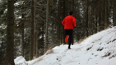 Winter trail running: man takes a run on a snowy mountain path in a pine woods. Stock Footage