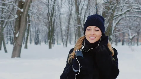 Winter walk - young woman walking in the park, listening to music on headphones Stock Footage