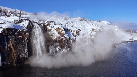 Winter waterfall cascading into freezing river with steam clouds Stock Footage 346324040