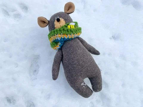 Wintertime teddy bear. Knitted bear toy laying over snow background. Stock Photos