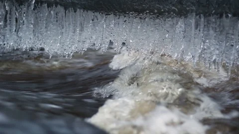 Wintry river flows fast after a spring thaw, with a row of icicles hanging do Stock Footage 126594783
