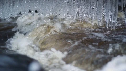 Wintry river flows fast after a spring thaw, with icicles hanging down above  Stock Footage 126594792