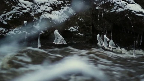 Wintry river flows fast after a spring thaw, with lumps of ice dangling on br Stock Footage 126594804