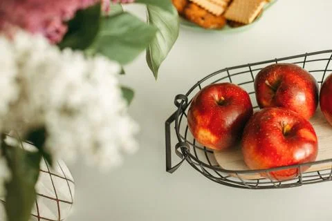 Wire Basket Filled With Apples Next to Vase of Flowers Stock Photos