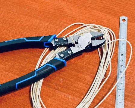 Wire cutters resting on wire coils with a metal ruler on a wooden workbench Stock Photos