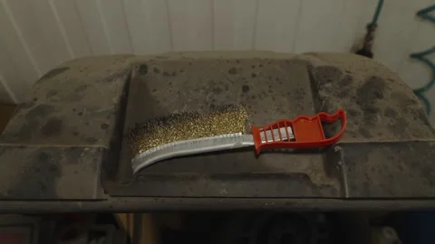 A wire scratch brush with an orange plastic handle lying on a dusty surface. Stock Footage 340558739