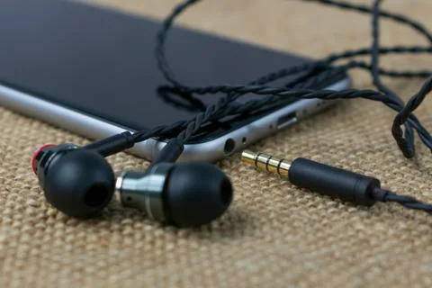Wired plug-in headphones with a plug, on the background of a smartphone outsi Stockfoto's