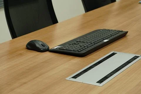 A wireless black mouse and a full-sized keyboard are placed on the wooden desk. Stock Photos
