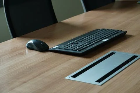 A wireless black mouse and a full-sized keyboard are placed on the wooden desk. Stock Photos