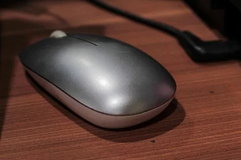 Wireless computer mouse resting on a wood desk surface for office equipment a Stock Photos