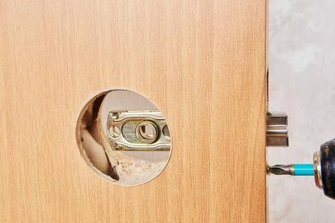 Wireless drill is used to secure latch plate with screws into door panel, a.. Stock Photos