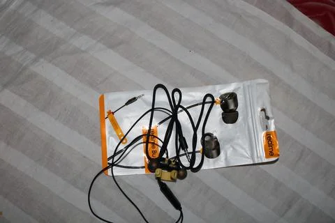 Wireless earbuds and charging cable on a white and gray striped cloth Foto stock