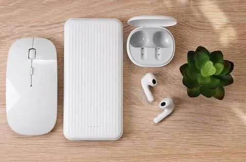 Wireless earbuds with charging case and computer mouse on wooden desk Stock Photos