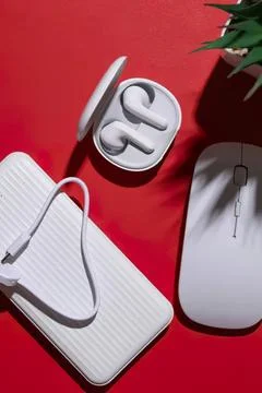 Wireless earbuds with charging case next to computer mouse and plant Stock Photos