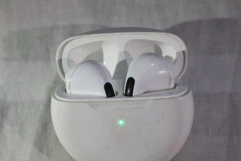 Wireless earbuds in white charging case with green light on front Foto stock