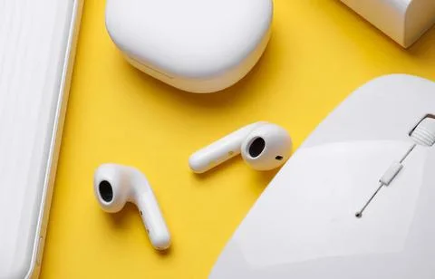 Wireless earbuds on yellow surface with mouse and headphones Stock Photos