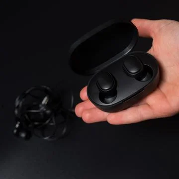 Wireless headphones in hand. Bluetooth vs  wired headphones. Stock Photos