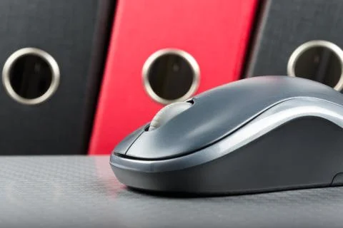 A wireless mouse placed on notebook and three folders in the background Stock Photos