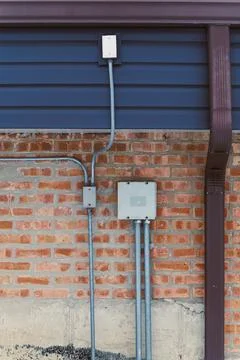 Wires and boxes connected to brick wall and siding on a building in a resid.. Stock Photos