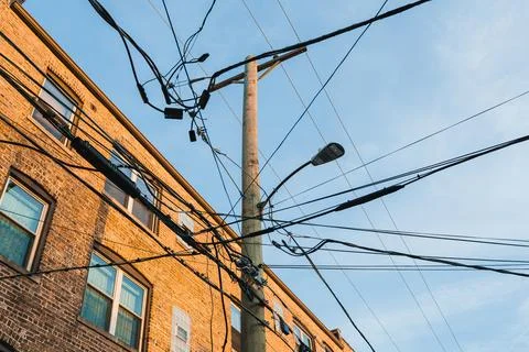 Wires stretch between a utility pole and nearby brick buildings in a city. Th Stock Photos