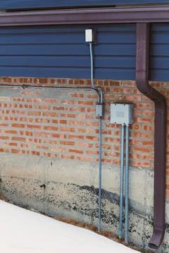 Wiring and utility boxes attached to a brick wall with a snow-covered groun.. Stock Photos