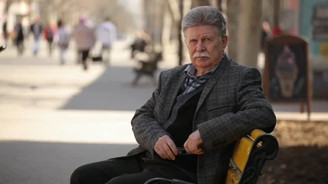 A wise man with a white mustache sits on a bench and enjoys the spring Video stock 88449481