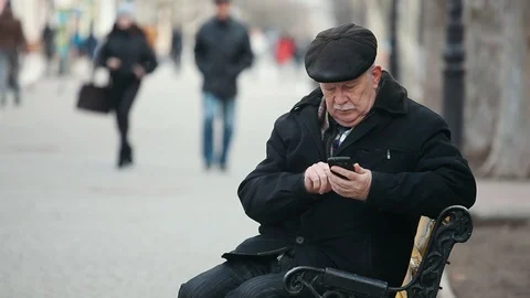 A wise old man sits on a bench and dials his mobile in a park alley in autumn Stock-Footage 85573749