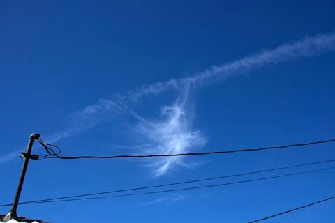 Wisps of cloud drift above power lines. Stock Photos