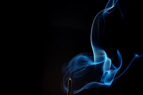 Wispy blue smoke wave flowing against a black background, creating a sense .. Stock Photos