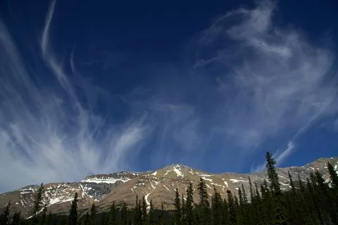 Wispy Cirrus Clouds Dance Over Rugged, Snow-Dusted Mountain Peaks Stock Photos