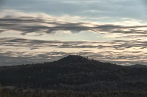 Wispy, wavy clouds over mountain peak Stock Photos