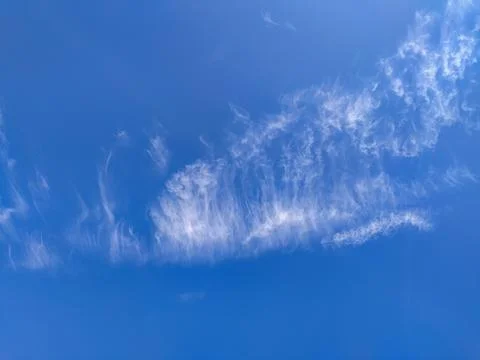 Wispy white cirrus clouds drift across a vibrant blue sky, evoking a sense of Stock Photos