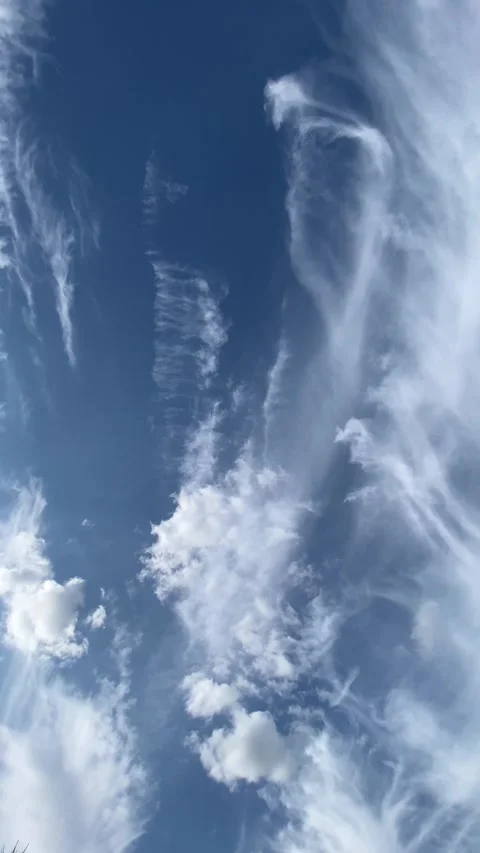 Wispy white clouds dancing and morphing against vibrant blue sky 動画素材 303210222