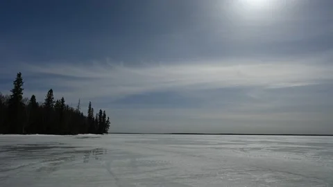 Wispy white clouds drift through a blue sky above a frozen lake  Stock Footage 152483045