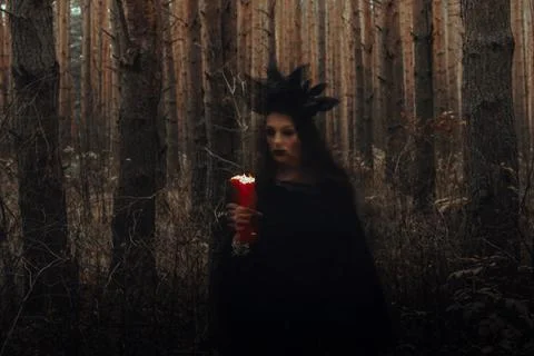 Witch in a black costume performs dark spells with candles in the forest Stock Photos